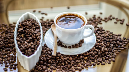 Black coffee in white cup with roasted beans around on glass table. First drink in the morning, black coffee. A cup of coffee and coffee beans on glass background with copy space.