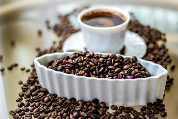 Black coffee in white cup with roasted beans around on glass table. First drink in the morning, black coffee. A cup of coffee and coffee beans on glass background with copy space.