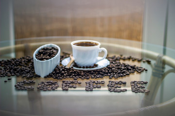 Mug coffee and coffee inscription from coffee grains. Bright background, cup and white bowl full of beans. Morning routine. Word coffee made of beans, coffee mug for coffee on glass table. Copy-space.