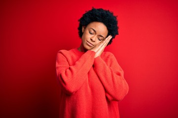 Fototapeta na wymiar Young beautiful African American afro woman with curly hair wearing casual sweater sleeping tired dreaming and posing with hands together while smiling with closed eyes.