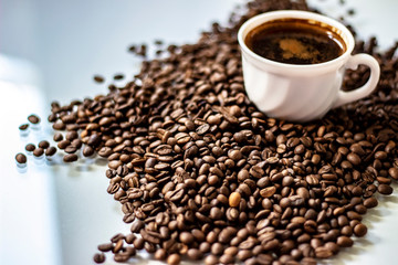 Coffee cup and beans on a white background. A cup of tasty drink and coffee grains. Coffee cup and coffee beans on white board. White cup of black coffee with roasted coffee beans. Space for text.