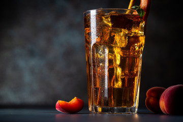 Glass of peach or apricot iced tea with fruit slices against dark blue background