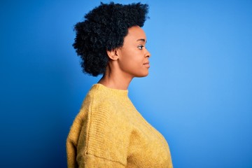 Fototapeta na wymiar Young beautiful African American afro woman with curly hair wearing yellow casual sweater looking to side, relax profile pose with natural face and confident smile.