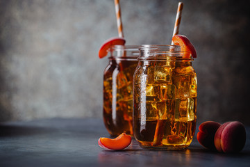 Glass of peach or apricot iced tea with fruit slices against dark blue background