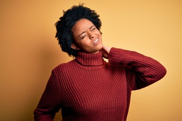 Young beautiful African American afro woman with curly hair wearing casual turtleneck sweater Suffering of neck ache injury, touching neck with hand, muscular pain