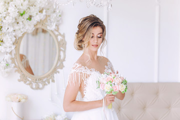 Beautiful bride with a wedding bouquet in a beautiful white room, catalog of wedding dresses, beautiful bride waiting for the groom, portrait of the bride, single bride in a beautiful dress