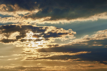 Beautiful blue sunset sky with beams of the sun that hid behind textured clouds