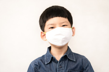 Portrait of cute little Asian boy wear medical face mask in daily life to protect from coronavirus during Covid-19 pandemic and social distancing. Stay safe & new normal for school student concept