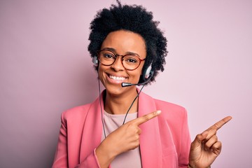 Young African American call center operator woman with curly hair using headset smiling and looking...