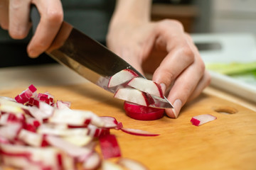 Women's hands slice radishes with a knife on a wooden Board close up