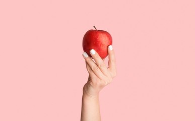 Female hand holding ripe red apple on pink background, close up. Panorama - Powered by Adobe
