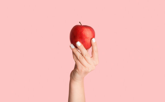 Female hand holding ripe red apple on pink background, close up. Panorama
