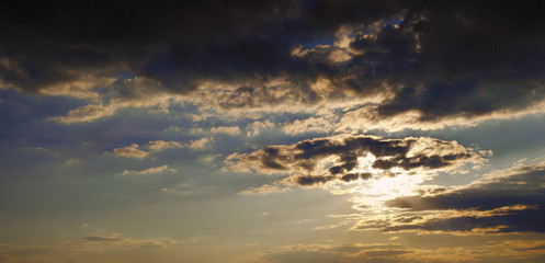 Panoramic photo of beautiful blue sunset sky with beams of the sun that hid behind textured clouds