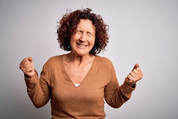 Middle age beautiful curly hair woman wearing casual sweater over isolated white background very happy and excited doing winner gesture with arms raised, smiling and screaming for success. Celebrate