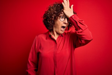 Fototapeta na wymiar Middle age beautiful curly hair woman wearing casual shirt and glasses over red background surprised with hand on head for mistake, remember error. Forgot, bad memory concept.