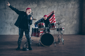 Photo of two retired people rock band group perform concert play drum instruments sing mic hold usa flag patriotic party wear rocker leather outfit isolated grey concrete wall background