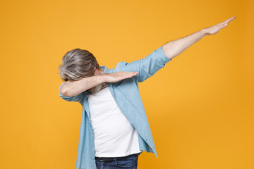 Elderly gray-haired mustache bearded man in casual blue shirt posing isolated on yellow background studio portrait. People emotions lifestyle concept. Mock up copy space. Showing DAB dance gesture.