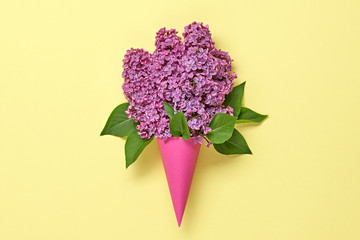 Blossom spring bouquet in ice cream cone. Pink lilac bloom flowering, top view. Minimal creative concept. Springtime lilac blooming. Trendy yellow vivid fashionable design.