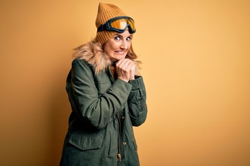 Middle age beautiful blonde skier woman wearing snow sportwear and ski goggles laughing nervous and...