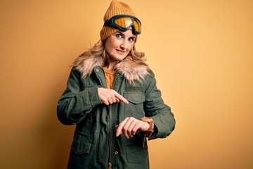 Middle age beautiful blonde skier woman wearing snow sportwear and ski goggles In hurry pointing to watch time, impatience, upset and angry for deadline delay