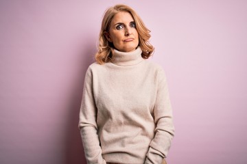 Obraz premium Middle age beautiful blonde woman wearing casual turtleneck sweater over pink background Relaxed with serious expression on face. Simple and natural looking at the camera.