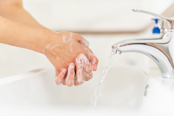 Man or woman washes hands with soap while standing at the sink in the bathroom.