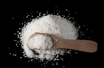 Shredded coconut meat, powder pile with wooden spoon isolated on black background