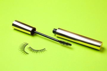 Mascara with fake eyelashes on color background