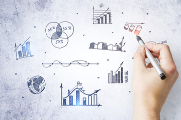 Businessman hand drawing charts and graphs on concrete wall