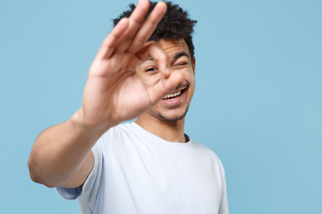 Smiling young african american guy in casual white t-shirt posing isolated on blue background....