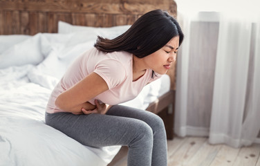 Asian Girl Having Abdominal Pain Sitting In Bed At Home
