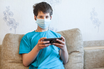 Fototapeta premium Preteen boy wearing medical mask listening music with earphones and cellphone while sitting on couch in domestic room