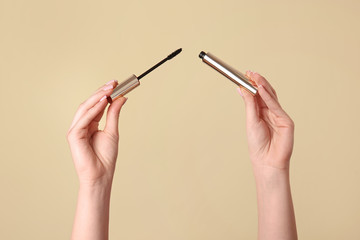 Female hands with mascara on color background