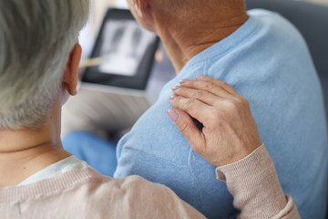 Close up of senior woman supporting husband during visit to medical clinic, focus on female hand on...