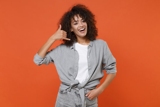 Cheerful young african american woman girl in gray casual clothes isolated on orange background studio portrait. People lifestyle concept. Mock up copy space. Doing phone gesture says call me back.