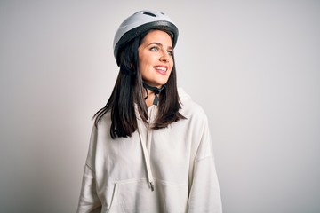 Young cyclist woman with blue eyes wearing bike helmet over isolated white background looking away to side with smile on face, natural expression. Laughing confident.