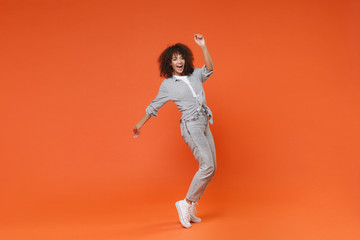 Fototapeta na wymiar Funny young african american woman girl in gray casual clothes posing isolated on orange background in studio. People lifestyle concept. Mock up copy space. Dancing, standing on toes, rising hands.