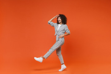 Fototapeta na wymiar Excited young african american woman girl in gray casual clothes posing isolated on orange background. People lifestyle concept. Mock up copy space. Holding hand at forehead looking far away distance.