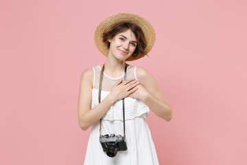 Pleasant pretty young tourist girl in dress hat with photo camera isolated on pink background. Female traveling to travel weekends getaway. Air flight journey concept. Put folded hands on chest heart.