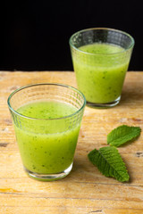Top view of two glasses of cucumber juice with mint leaves on rustic table, black background, vertical