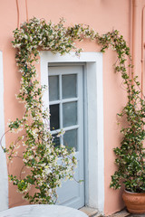 Fototapeta na wymiar Soft beautiful colorful house facade and white blossom flower arch over door. Traditional greek house with blooming flowers in Corfu island, Greece. Vertical. 