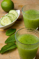 Aerial view of two glasses of cucumber juice with mint leaves, slices and lime, with selective focus, on rustic table, vertical