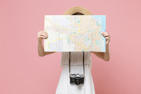 Young tourist woman in summer white dress hat with photo camera isolated on pink background. Female traveling abroad to travel weekend getaway. Air flight journey concept. Covering face with city map.