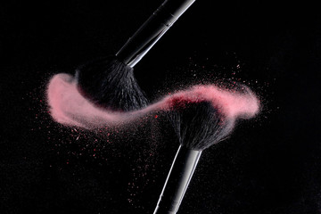 Makeup brushes with colorful powder explosion on black background. High speed photography of...