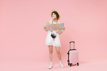 Smiling tourist girl in dress hat with suitcase photo camera isolated on pink background. Female traveling abroad to travel weekends getaway. Air flight journey concept. Hold city map, looking aside.
