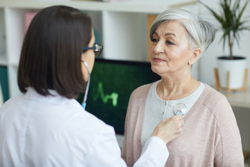 Portrait of female doctor listening to heart and breathing of senior woman via stethoscope on chest...
