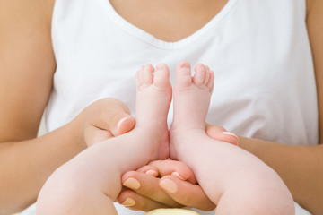 Young mother hands holding her infant little feet. Playing with baby. Lovely, emotional moment. Relationship concept. Closeup.
