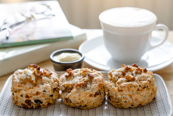 Traditional British cheese scones with blurry cup of coffee and  book background, freshly baked scones english buns with bright light morning  or afternoontea in spring or summer