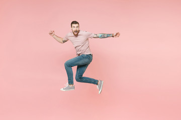 Fototapeta na wymiar Side view of shocked young tattooed man guy in pastel casual t-shirt posing isolated on pink background studio. People lifestyle concept. Mock up copy space. Jumping, spreading hands, looking camera.
