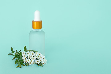 Fototapeta na wymiar Glass cosmetik bottle with oil. container for a product for women with small white flowers on a turquoise background. Cosmetic jar. Place for text